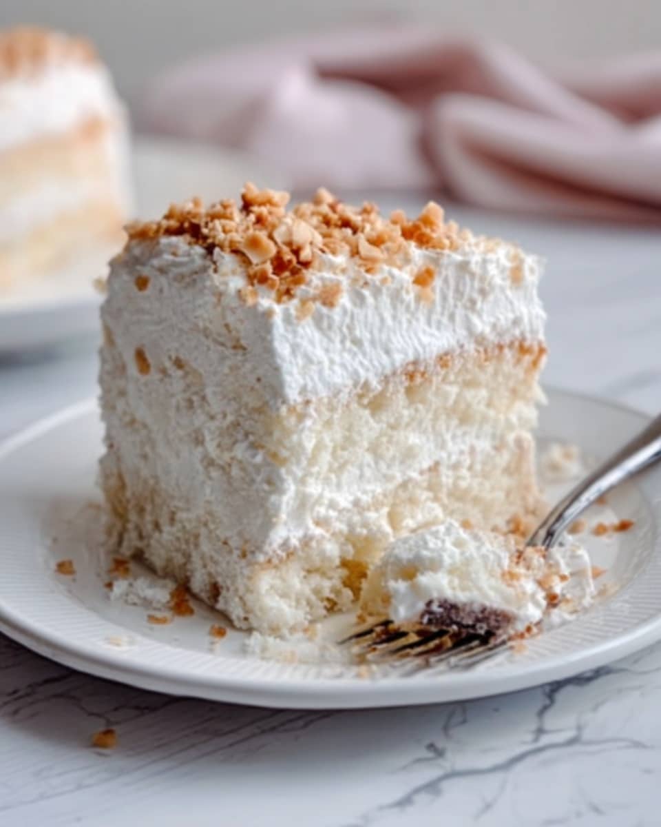 The image shows a slice of creamy white layered cake on a white plate placed on a white marbled surface. The cake has three layers: a soft, moist white base, a thick middle layer of smooth white cream or filling, and a fluffy top layer covered with white whipped cream. Small crumbs of light brown nuts or toffee pieces are sprinkled evenly over the top cream. A silver fork lies on the plate, with a small bite of the cake on its prongs, resting near the slice. A woman's hand is not visible, but the setting looks simple and clean. Photo taken with an iphone --ar 4:5 --v 7