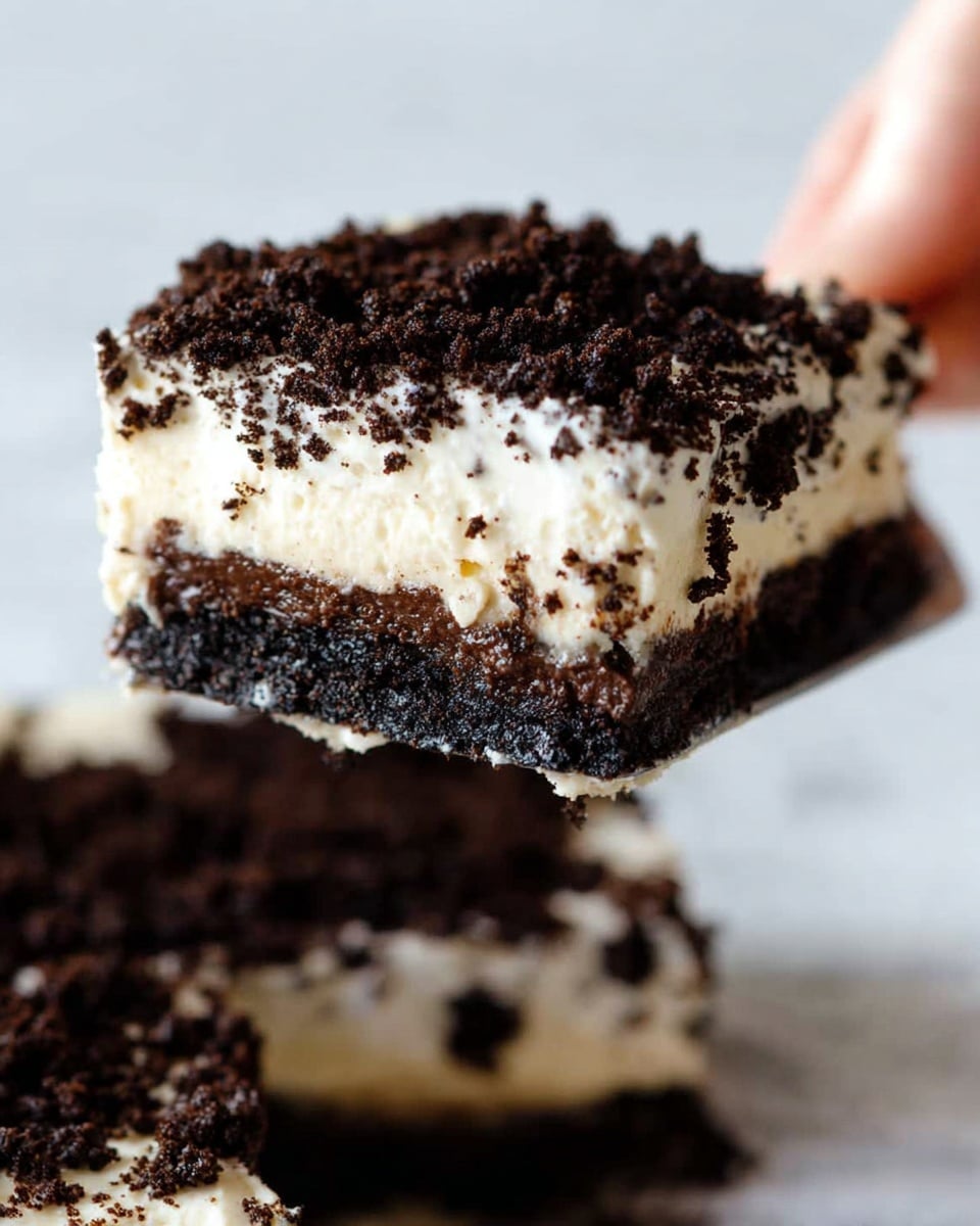 A close-up view of a layered dessert being lifted by a woman's hand, showing a thick bottom layer of dark chocolate crumbs, a middle creamy white layer, topped with another thick layer of dark chocolate crumbs with a crumbly texture, placed against a white marbled background. Photo taken with an iphone --ar 4:5 --v 7