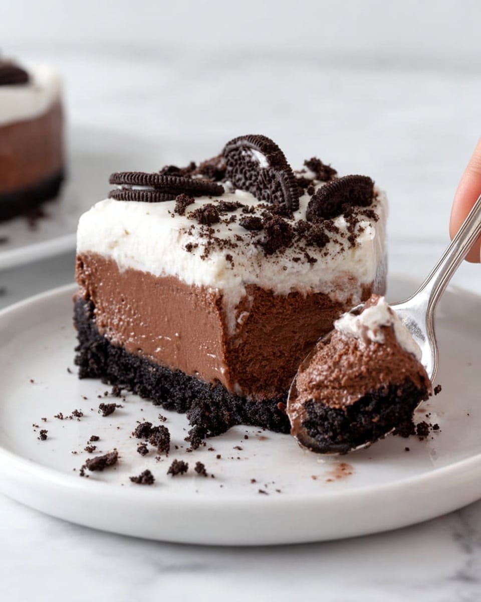 A round dessert with three clear layers in a glass pie dish placed on a white marbled surface. The bottom layer is dark and crumbly, made of crushed chocolate cookies forming a solid base. The middle layer is thick, smooth, and dark brown, resembling a rich chocolate pudding. The top layer is fluffy and white, like whipped cream, sprinkled with small and large pieces of crushed chocolate cookies scattered unevenly. Some cookies are broken with visible white filling. The whipped cream has soft, wavy peaks. In the background, there is a white cloth and a few whole chocolate sandwich cookies. Photo taken with an iphone --ar 4:5 --v 7