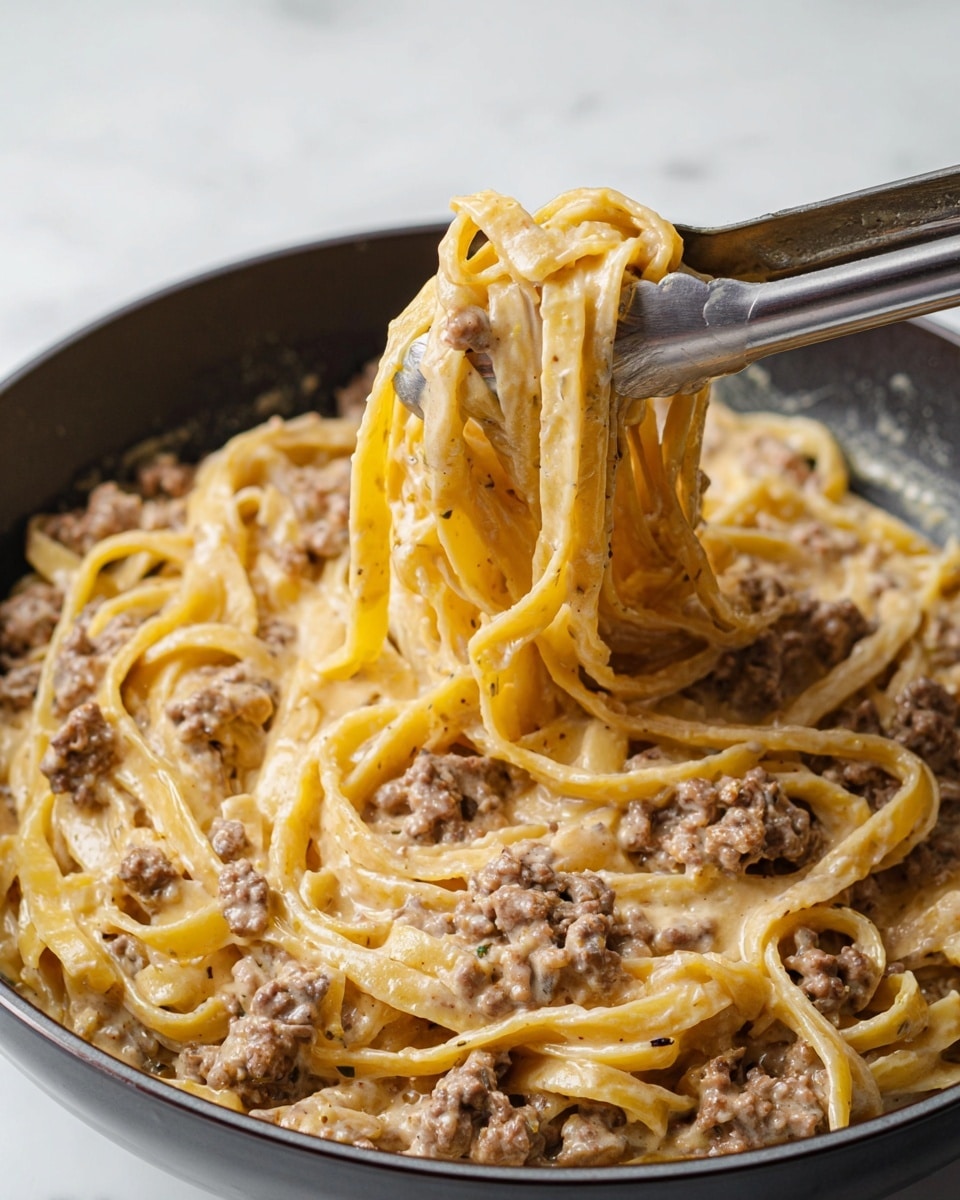 The image shows a close-up of creamy pasta with small bits of ground meat mixed in. The pasta is long and flat, like fettuccine, coated in a thick, beige creamy sauce with visible specks of meat spread evenly throughout. The pasta is lifted by metal tongs in the center, showing the texture of the noodles and meat clearly. The dish is in a dark bowl, set on a white marbled surface, highlighting the rich sauce and meatiness of the pasta. photo taken with an iphone --ar 4:5 --v 7