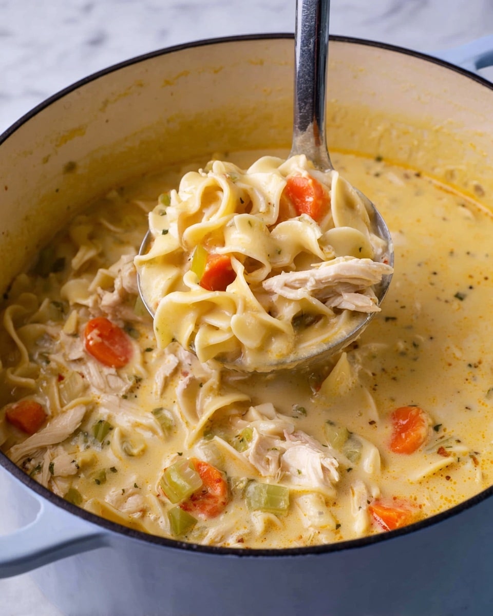 The image shows a large white pot filled with a thick, creamy yellow soup. Inside the soup, there are multiple layers including wide egg noodles that are soft and slightly curled, small orange carrot cubes, light green celery pieces, and chunks of white meat. The soup looks smooth and rich, coating the ingredients well. A ladle is lifting a portion of the soup, showing the mix of noodles, vegetables, and meat all together. The background surface is a white marbled texture. photo taken with an iphone --ar 4:5 --v 7