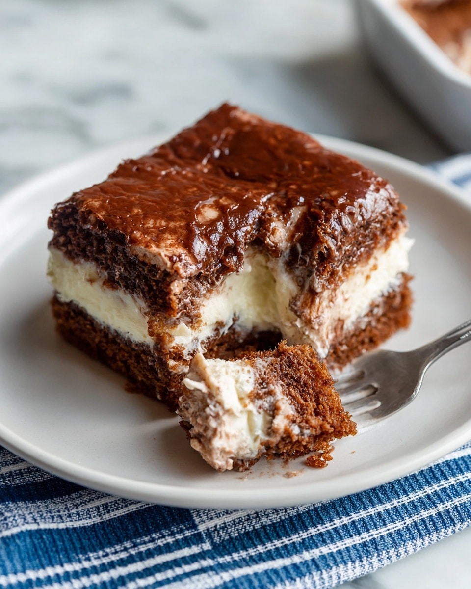 A square piece of chocolate and cream layered dessert rests on a white plate, showing three clear layers: a top dark brown, slightly cracked cake layer with a crisp texture, a middle creamy white layer that looks soft and thick, and a bottom dense chocolate layer. A fork with a small bite of the dessert lifts some of the creamy white and chocolate layers. The plate sits on a white marbled surface with a blue and white striped cloth partially visible underneath. Photo taken with an iphone --ar 4:5 --v 7