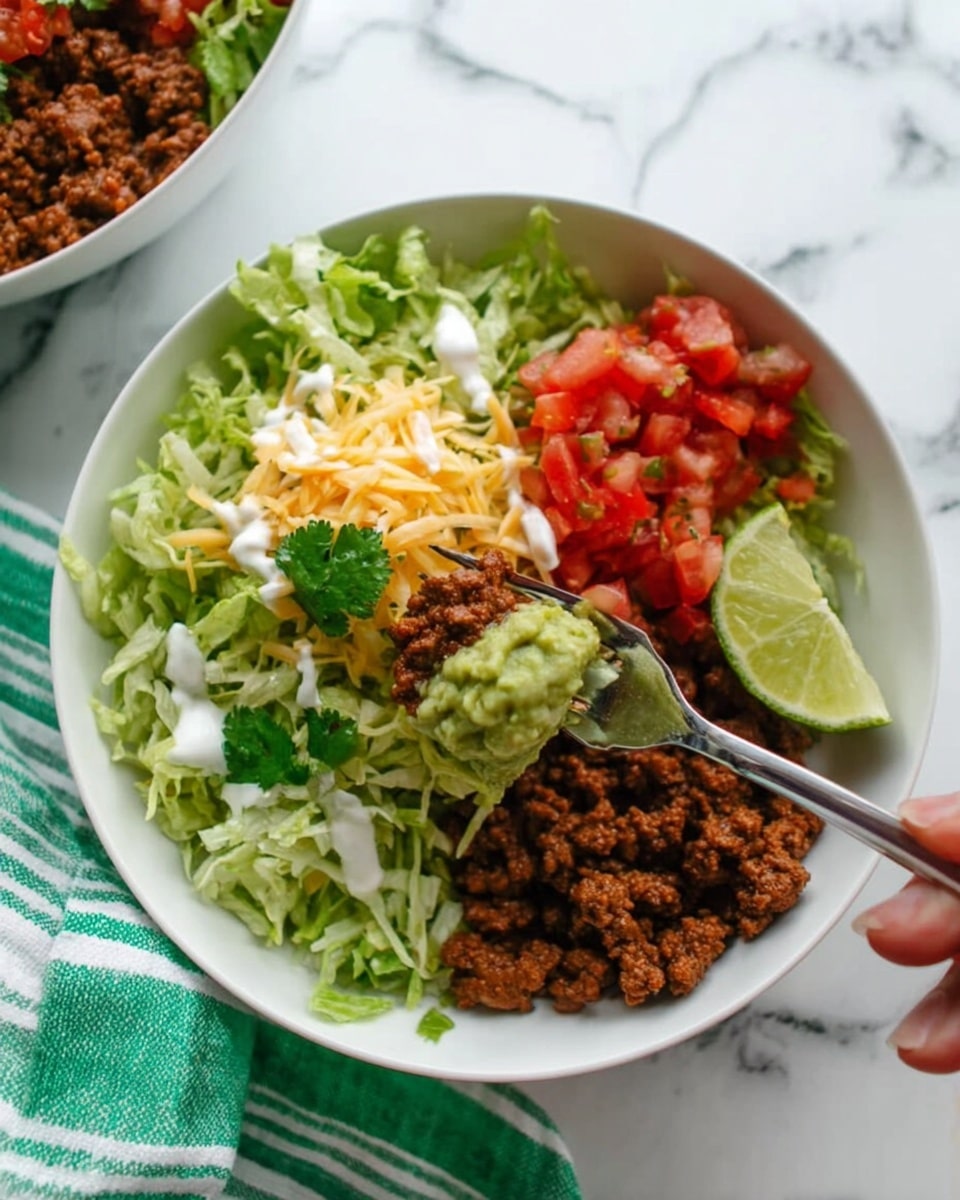 A white bowl with layers starting at the bottom with shredded lettuce and some finely chopped cilantro, topped by a generous layer of cooked ground beef with a rich brown color. Around the meat, there are small sections of creamy guacamole in light green, bright red salsa, diced red tomatoes, and shredded yellow cheese. A wedge of lime rests on the edge of the bowl. A woman’s hand holds a fork scooping a mix of lettuce, ground beef, and white sauce above the bowl. The bowl sits on a white marbled surface with a folded green and white striped cloth nearby. Photo taken with an iphone --ar 4:5 --v 7