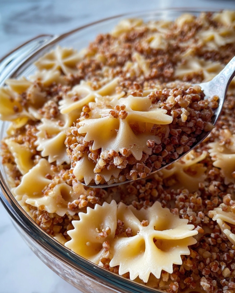 The image shows a close-up of a clear glass dish filled with two main layers: a base layer of light beige bow-tie shaped pasta with smooth texture and slightly curved edges, and a thick top layer of small, grain-like buckwheat with a rough, uneven texture in shades of brown and light tan. A metal spoon is scooping a mix of both buckwheat and pasta, showing the size and texture contrast; the buckwheat grains appear grainy and slightly crumbly while the pasta is smooth and soft. The dish sits on a white marbled surface, enhancing the warm tones of the food. photo taken with an iphone --ar 4:5 --v 7