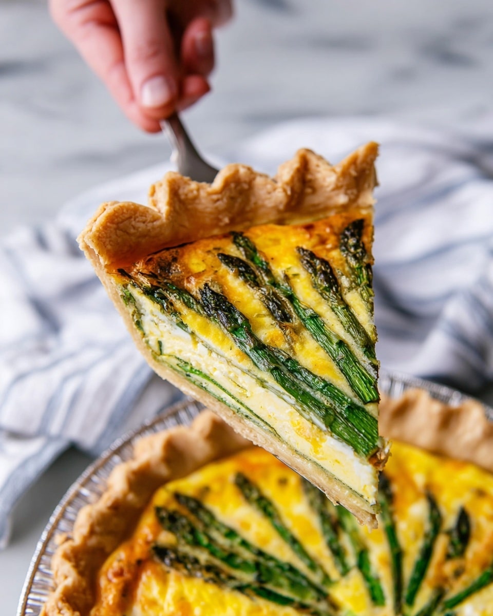 A slice of quiche is held up by a woman's hand using a metal spatula. The quiche has a thick, golden-brown, flaky crust with detailed crimping on the edge. Inside, the filling shows a bright yellow custard base with layered green asparagus spears placed evenly on top, their tips dark green and slightly roasted. The quiche is in a silver baking dish, sitting on a white marbled surface with a soft, white, and light blue striped cloth blurred in the background. The slice is fresh and moist with a smooth texture. Photo taken with an iphone --ar 4:5 --v 7