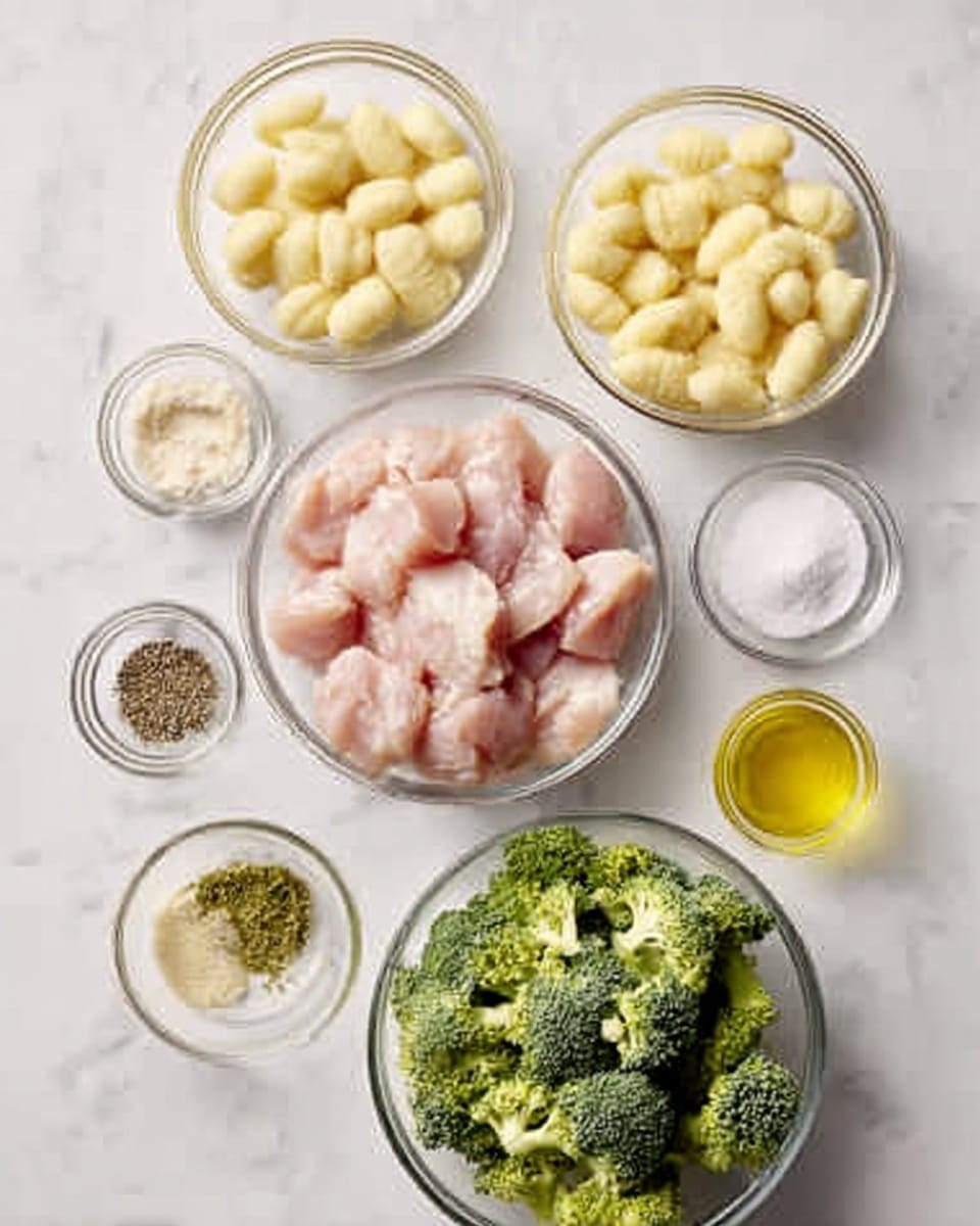 The image shows several clear glass bowls arranged on a white marbled surface. In the center, there is a bowl filled with chunks of raw chicken, light pink in color. Above it, a bowl contains small pale yellow gnocchi. To the right of the chicken, there are small bowls with a creamy white sauce, a pale beige powder, and granulated salt. To the left of the chicken are bowls with dark black pepper, light green seasoning, and crushed garlic. Below the chicken, a large bowl holds bright green broccoli florets. A small bowl with a golden yellow liquid, likely oil, is placed near the top left. The overall look is clean and organized with fresh ingredients. Photo taken with an iphone --ar 4:5 --v 7