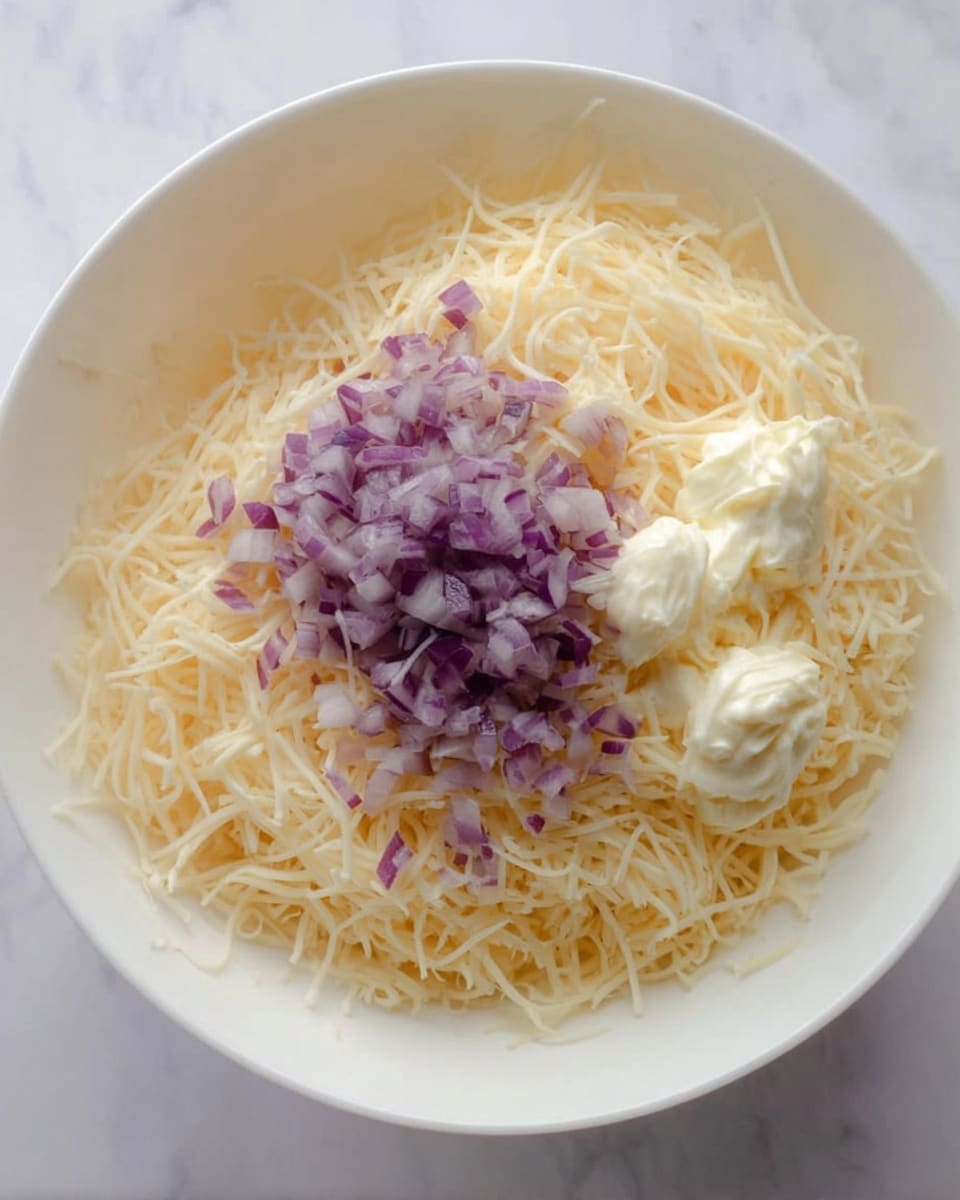 A white bowl filled with a large layer of fine shredded pale yellow cheese covering most of the bowl's base, topped slightly off-center with a pile of small, diced purple onion pieces and two generous dollops of creamy white mayonnaise on the right side. The bowl is set on a white marbled surface. Photo taken with an iphone --ar 4:5 --v 7