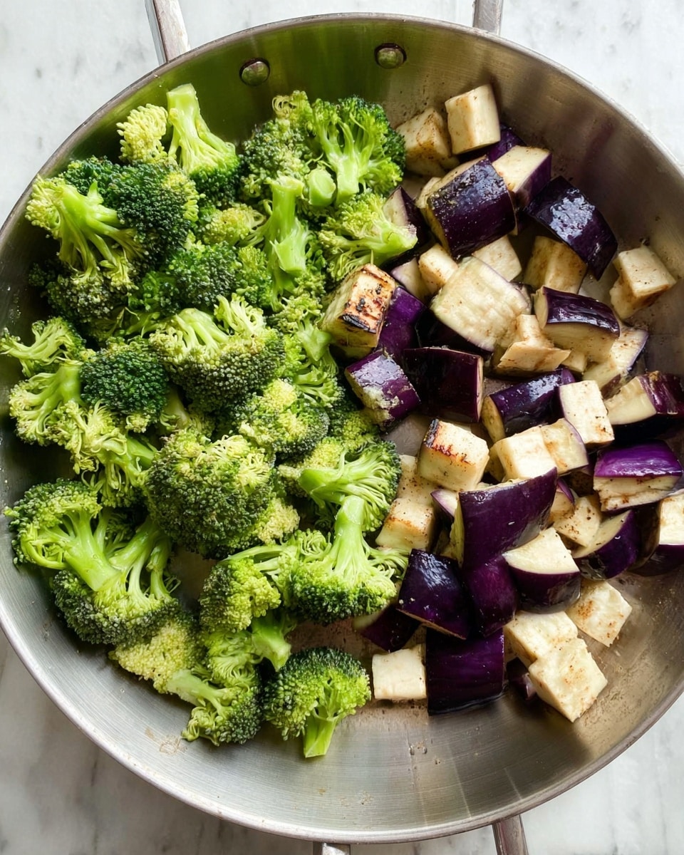 A silver pan filled with a mix of fresh vegetables, featuring bright green broccoli florets on one side and roughly chopped eggplant pieces with deep purple skin and creamy white flesh on the other side, resting on a white marbled surface. The broccoli has a rough texture with tiny buds, while the eggplant chunks show some grill lines and seed spots. The vegetables are raw and evenly spread inside the pan. Photo taken with an iphone --ar 4:5 --v 7