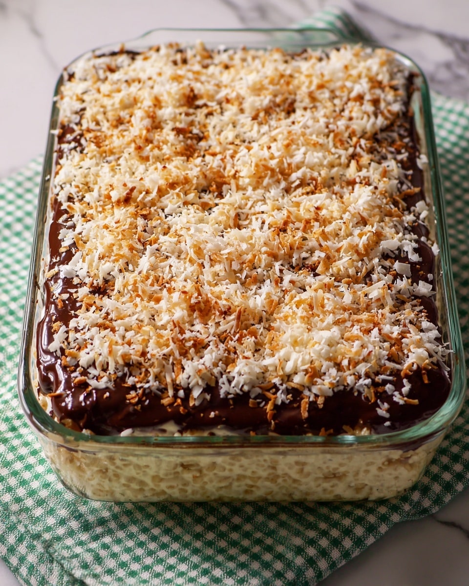 A rectangular clear glass dish holds a layered dessert placed on a green and white checkered cloth over a white marbled surface. The bottom layer is light and fluffy, made from puffed rice cereal, creamy and pale beige in color. The middle layer is thick, unevenly spread melted dark chocolate with a rich, glossy texture and dark brown color. The top layer is covered with toasted shredded coconut, showing a mix of light beige and golden brown shades with a slightly crunchy texture. The layers are visible from above, with the top coconut layer sprinkled evenly but with some gaps revealing chocolate beneath. Photo taken with an iphone --ar 4:5 --v 7