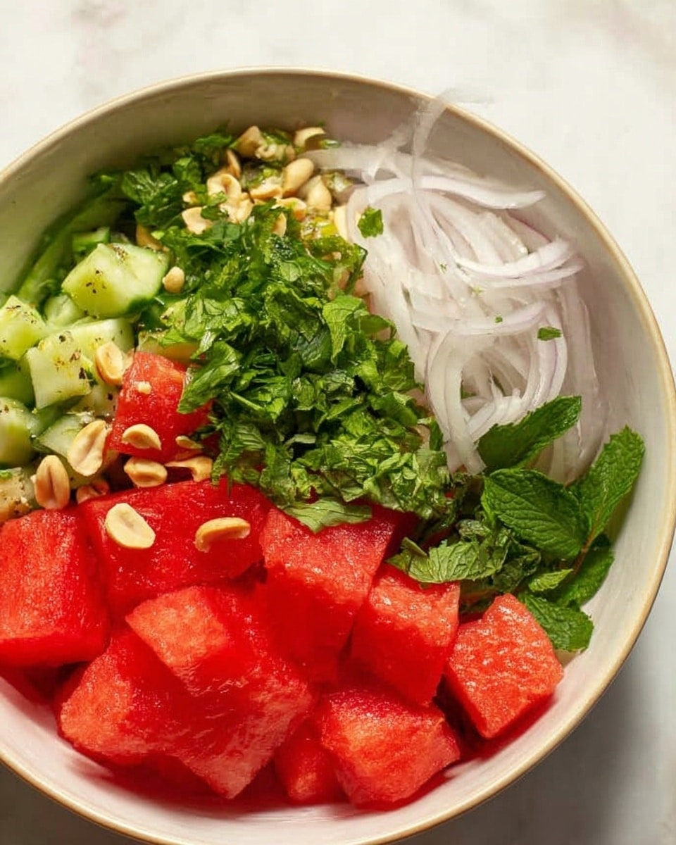 The image shows a white bowl filled with a colorful salad made of several layers and ingredients. On the top right are thin, white slices of onion that look slightly curled, next to bright green mint leaves also finely chopped. Below and to the left are large, bright red cubes of watermelon with a juicy texture. At the bottom left, there are small green pieces that look like cucumber slices with some green herbs sprinkled over them, and small light brown nuts scattered around the salad. The bowl is placed on a white marbled surface. photo taken with an iphone --ar 4:5 --v 7