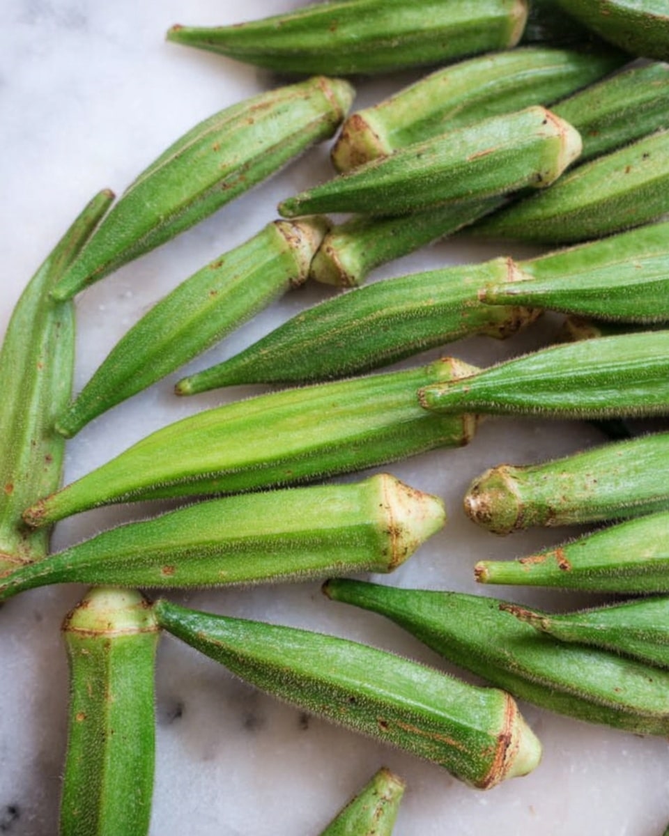 The image shows many fresh green okra pods arranged close to each other on a white marbled surface, with their tips and stems visible. The okra pods have a slightly fuzzy texture and a vibrant green color, with some light brown specks near the stems. The overall scene is bright and simple, focusing on the natural look of the okra pods. photo taken with an iphone --ar 4:5 --v 7
