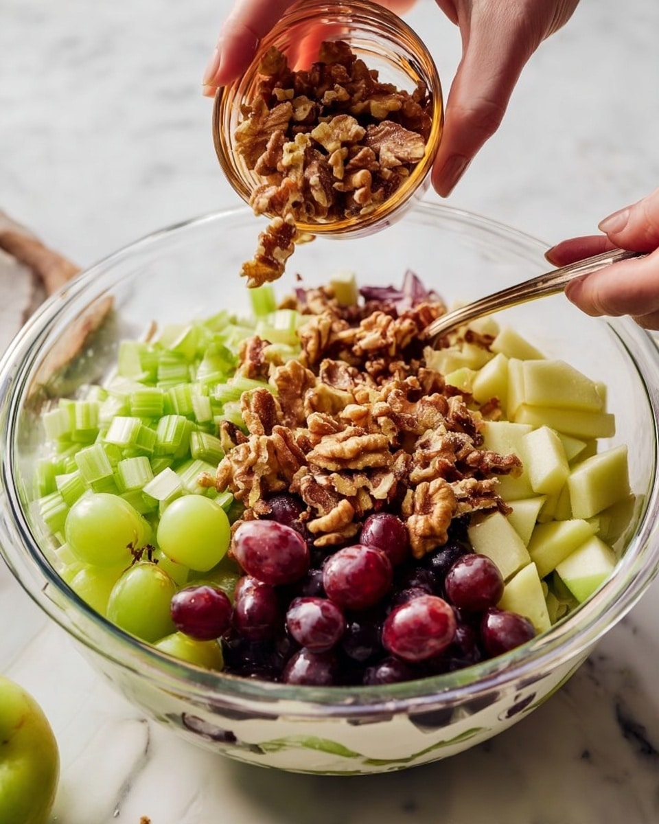 A clear glass bowl shows a layered salad with a white creamy base at the bottom, topped with chopped light green celery pieces on one side, and dark purple grapes cut in halves on another side. Light yellow-green apple cubes sit beneath the grapes, and a woman's hand pours rough walnut pieces from a small brown glass bowl onto the top. Another woman's hand holds a spoon mixing the salad, all placed on a white marbled surface. photo taken with an iphone --ar 4:5 --v 7