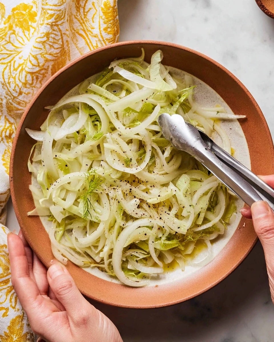 A close-up top view of a round light brown bowl filled with thin, pale yellow-green sliced fennel layers spread out unevenly inside. The fennel pieces show a mix of curved and straight shapes with some pieces overlapping. There are small black pepper sprinkles and a light coating of oil on the fennel slices. A woman's hand holds a pair of silver tongs on the right side of the bowl, gripping some fennel. Another woman's hand holds the bowl on the left side. The bowl is placed on a white marbled surface, with a yellow and white patterned cloth partially visible at the top. photo taken with an iphone --ar 4:5 --v 7