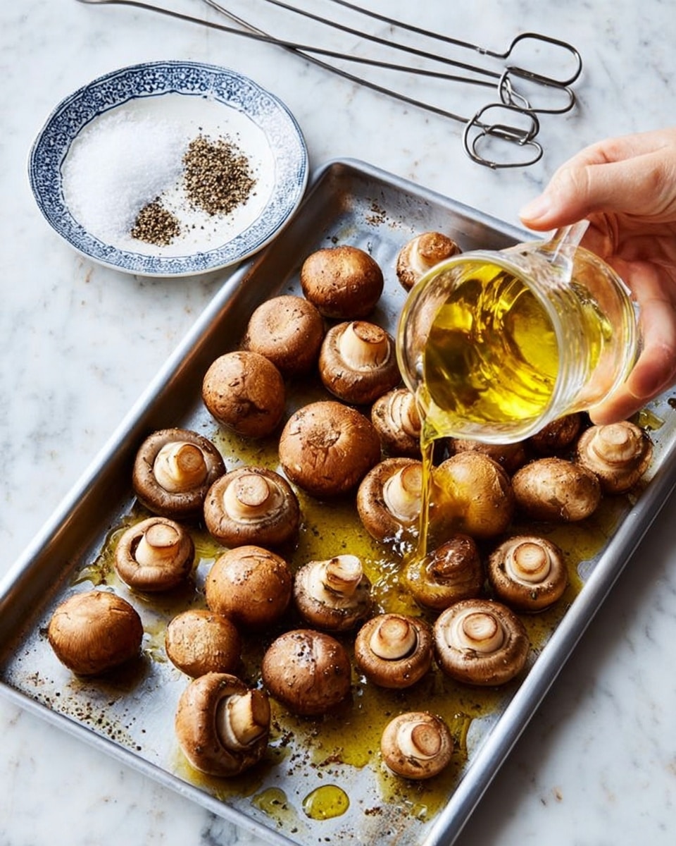A metal tray holds many small round brown mushrooms laid out evenly, some with tops facing up showing a smooth texture and some with bottoms visible showing light gills. A woman's hand is pouring golden oil from a clear measuring cup over the mushrooms, causing the oil to shine and spread in small pools on the tray. Above the tray, a white plate with blue patterns contains coarse salt and cracked black pepper, positioned near several thin metal skewers with looped ends, resting on a white marbled surface. photo taken with an iphone --ar 4:5 --v 7
