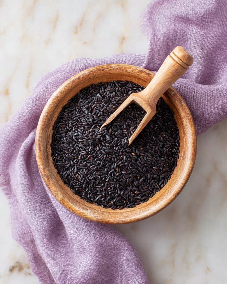 A light brown wooden bowl filled with many small, shiny black rice grains. A wooden scoop is inside the bowl, holding some black rice grains. The bowl sits on a soft purple cloth with a white marbled surface beneath it. photo taken with an iphone --ar 4:5 --v 7