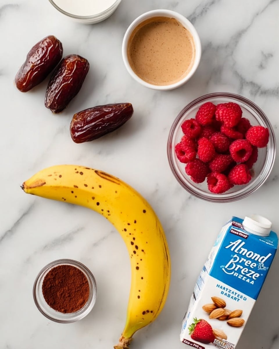 The image shows a white marbled surface with several food items neatly placed on it. In the center is a ripe yellow banana with small brown spots. Near the top left are two dark brown dates. Below the dates is a small white bowl filled with light brown almond butter. To the right of the banana are two small clear bowls: the top one contains red raspberries and the bottom one has bright red strawberries. Towards the bottom left are two glasses filled with almond milk, one partially visible. Near the bottom center is a small white dish with a heap of dark brown cocoa powder. At the bottom right is a blue and white carton of Almond Breeze vanilla almond milk. A woman's hand is not visible in this image. Photo taken with an iphone --ar 4:5 --v 7