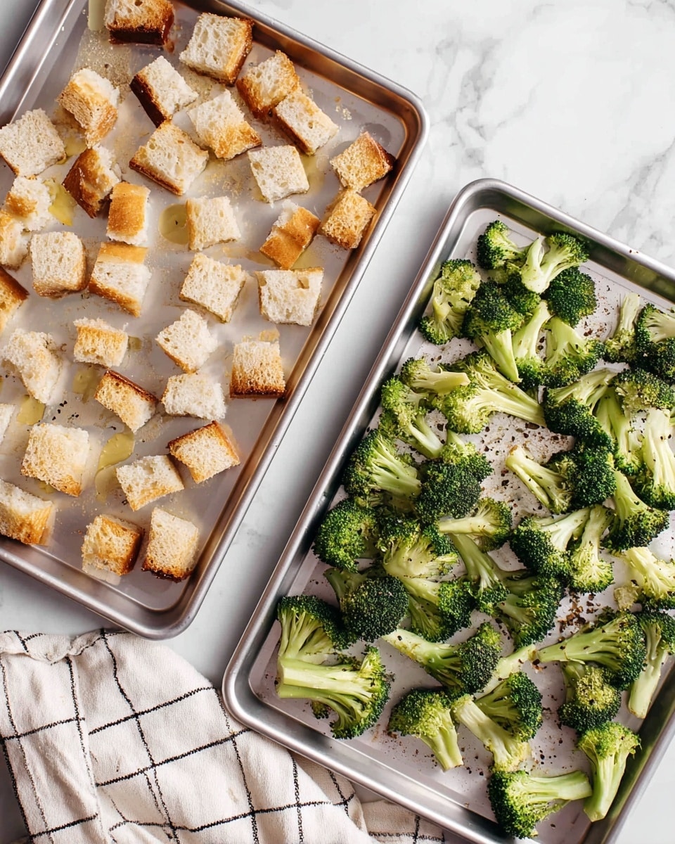 Two silver baking trays sit on a white marbled surface. The top tray holds one layer of small, square pieces of toasted bread with a golden brown color and light drizzle of oil. The bottom tray is filled with one layer of fresh broccoli florets showing a rich green color and sprinkled lightly with black pepper and oil. A cream cloth with a black grid design lies next to the trays. photo taken with an iphone --ar 4:5 --v 7
