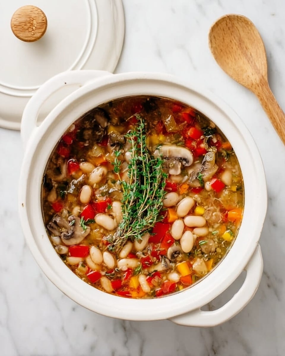 The image shows a white ceramic pot filled with a colorful vegetable and bean soup, placed on a white marbled surface. The soup has multiple layers visible: at the bottom are white beans, mixed with small cubes of red and yellow bell peppers, and chopped mushrooms, all floating in a clear broth with some green herbs sprinkled throughout. On top, a fresh sprig of green thyme rests in the center, adding a touch of natural texture. To the right of the pot lies a wooden spoon with a smooth surface. The pot’s lid is slightly visible in the upper left corner on the white marbled background. Photo taken with an iphone --ar 4:5 --v 7